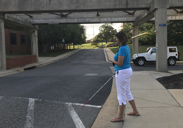 Three pictures show a student with a white cane, standing with one foot in the street.  A vehicle pulls out of the parking lot and waits while she crosses